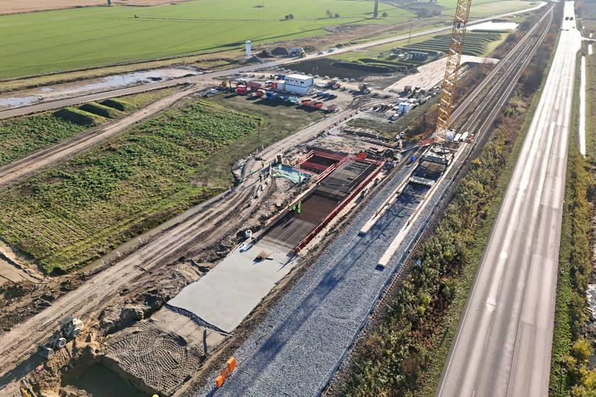 Man sieht Arbeiten mit Bewehrung für das Fundament der Brücke. Daneben steht ein Kran auf Schienen.