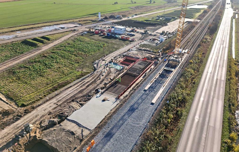 Man sieht Arbeiten mit Bewehrung für das Fundament der Brücke. Daneben steht ein Kran auf Schienen.