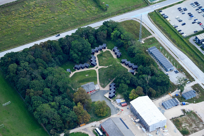 Campus Femern ligger mellem træerne. Bolighytterne ligger rundt om hovedhuset. Set fra luften.