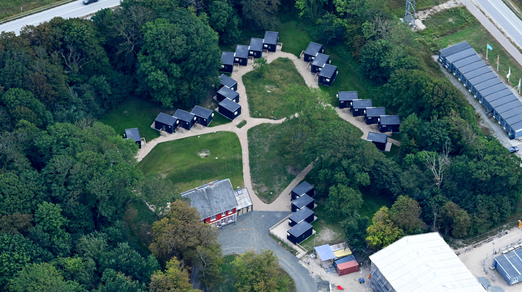 Udsigt fra oven over de små hytter på Campus Femern. Alle hytter er placeret rundt om en græsplæne.