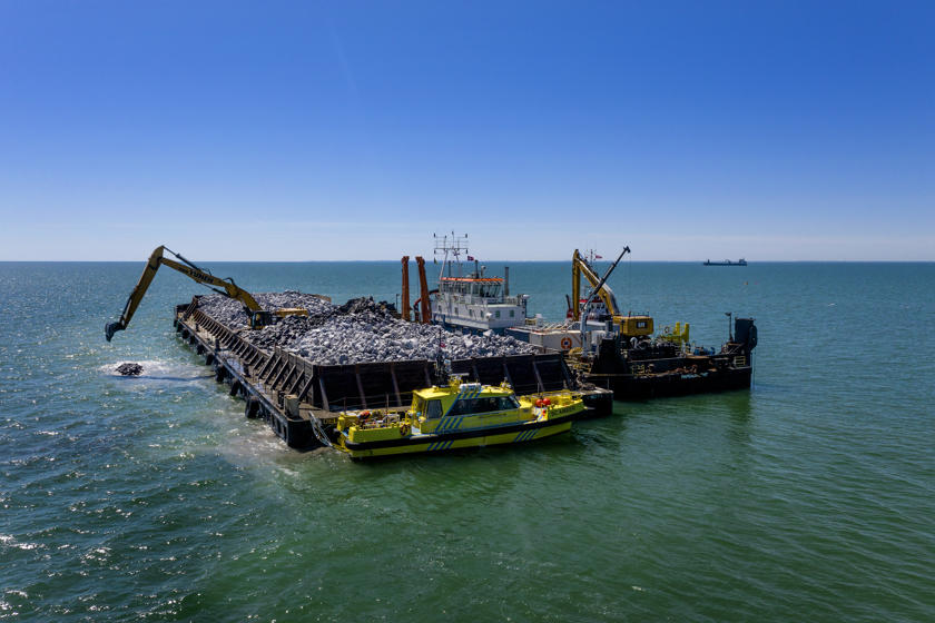 English: A barge with granit for the breakwaters in the Fehmarnbelt. Excavators drop the boulders into the sea to construct the breakwaters.//Dansk: En pram med granit til bølgebrydere i Fehmarnbelt. Gravemaskiner lægger kampestenene i havet for at bygge bølgebryderne.//Deutsch: Eine Schute mit Granit für die Wellenbrecher im Fehmarnbelt. Bagger versenken die Granitbrocken im Meer, um die Wellenbrecher zu errichten.