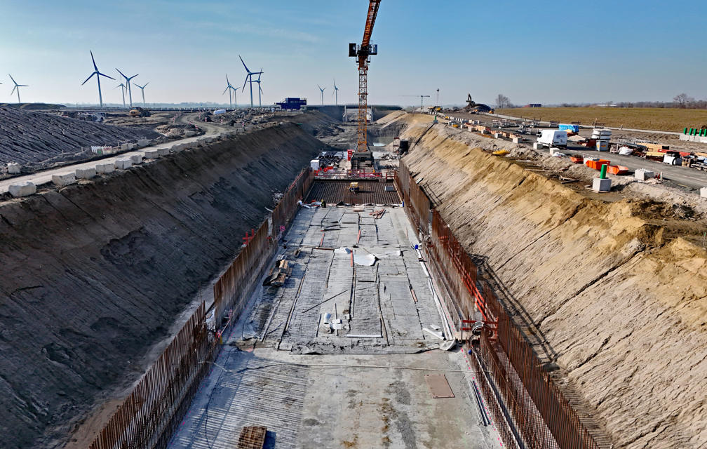 In dem ausgehobenen Trog ist bereits die Betonsohle für die Bahntrasse betoniert. Auf beiden Seiten ist die Bewehrung für die späteren Wände zu sehen.