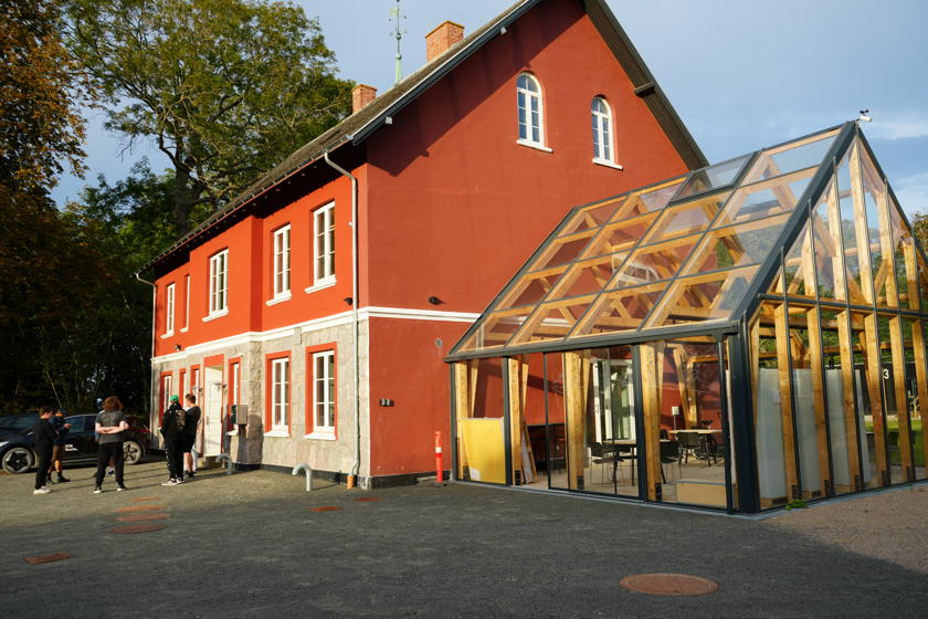 Det røde toetagers hovedhus med mange vinduer. På siden er der tilbygget en vinterhave.
