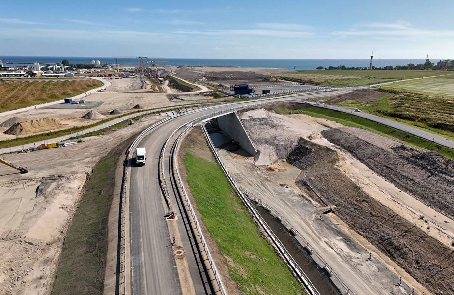 Im Bild ist eine Straße zu sehen, im Hintergrund das deutsche Tunnelportal. Die Straße führt über eine Brücke in Kurvenlage. 