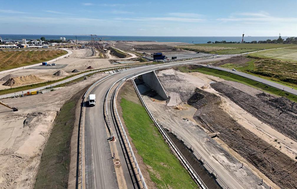 Im Bild ist eine Straße zu sehen, im Hintergrund das deutsche Tunnelportal. Die Straße führt über eine Brücke in Kurvenlage.