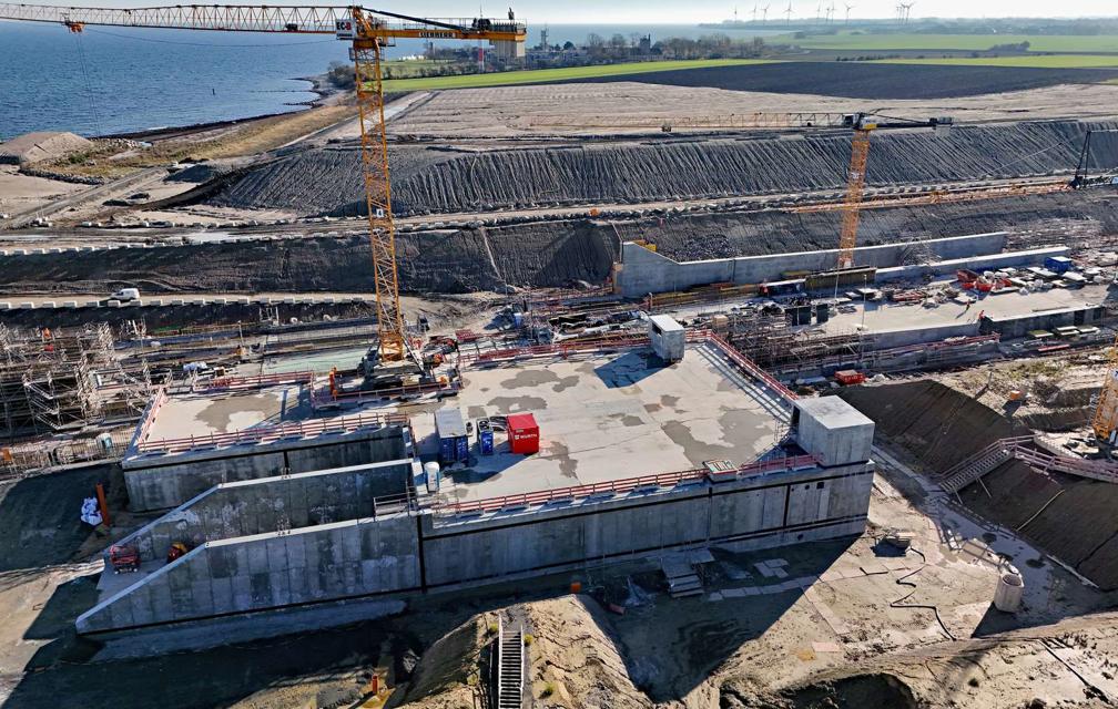 Im Vordergrund ist das Betriebsgebäude zu sehen: ein viereckiges Gebäude aus Beton. Daher entsteht aus Bewehrungsstahl und Beton die Tunneleinfahrt. Eine Außenwand ist angeschrägt, dort ist die Tunneleinfahrt.