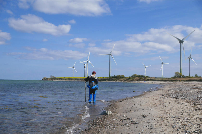 EN: A man is taking measurements while standing in the water on the beach at Fehmarn. // DK: En mand står i vandet ved stranden på Fehmarn og foretager målinger. // DE: Ein Mann nimmt im Wasser am Strand von Fehmarn stehend Messungen vor.