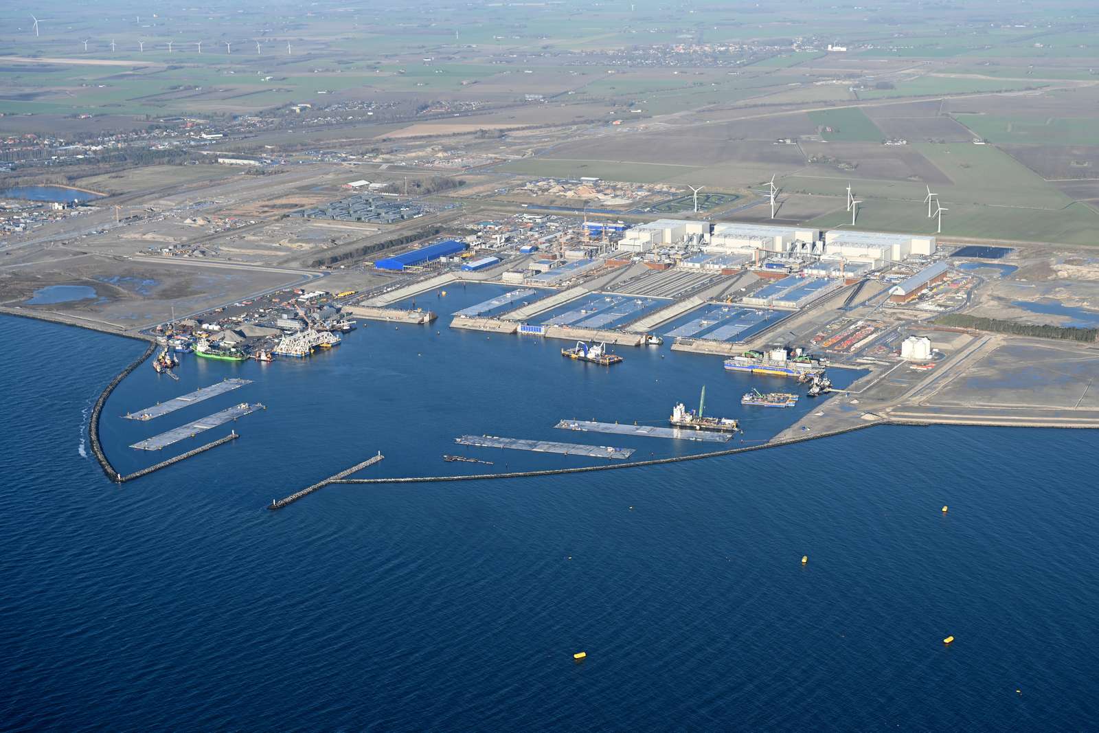 : The Danish tunnel construction site. Several work vessels and tunnel elements are moored in the working harbour.