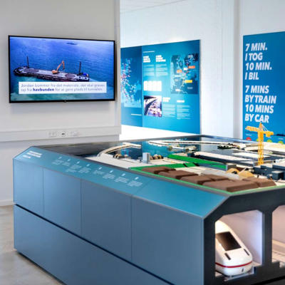 EN: Model of the tunnel factory in the exhibition in Rødbyhavn. Below are the tubes of the Fehmarnbelt tunnel, in which vehicles and trains travel. // DE: Modell der Tunnelfabrik in der Ausstellung in Rødbyhavn. Unten drunter werden die Röhren des Fehmarnbelt-Tunnel dargestellt, in denen Fahrzeige und Züge fahren. // DA: Model af tunnelfabrikken i udstillingen i Rødbyhavn. Nedenunder ses Femern Bælt-tunnelens rør, hvor biler og tog kører.