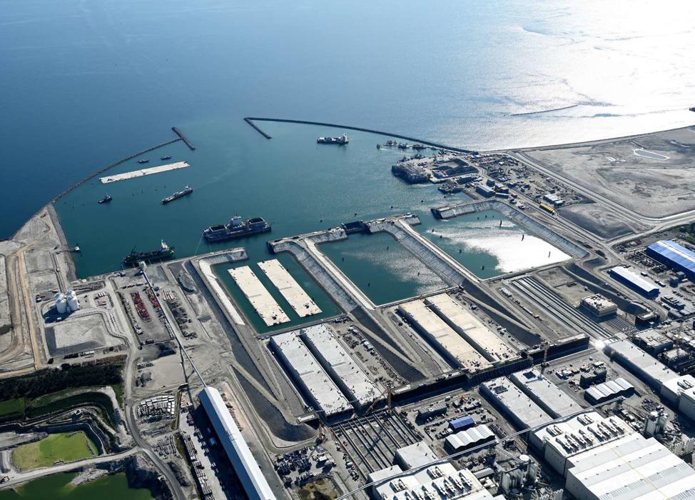 Elementer stikker ud af produktionshallerne. Foran hallerne ligger elementer, der skal færdiggøres. I bassinerne og i havnen flyder færdige elementer.