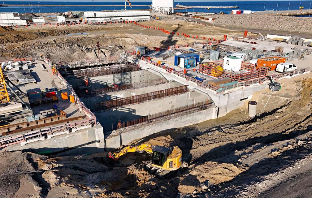 Das deutsche Tunnelportal. Eine Betonkonstruktion, an der an einer Stelle die Tunneldecke fehlt. Die Wände sind bereits betoniert. In der Baugrube ist außerdem ein Bagger zu sehen.