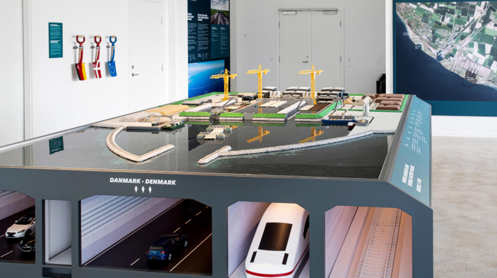 EN: Model of the tunnel factory in the exhibition in Rødbyhavn. Below are the tubes of the Fehmarnbelt tunnel, in which vehicles and trains travel. // DE: Modell der Tunnelfabrik in der Ausstellung in Rødbyhavn. Unten drunter werden die Röhren des Fehmarnbelt-Tunnel dargestellt, in denen Fahrzeige und Züge fahren. // DA: Model af tunnelfabrikken i udstillingen i Rødbyhavn. Nedenunder ses Femern Bælt-tunnelens rør, hvor biler og tog kører.
