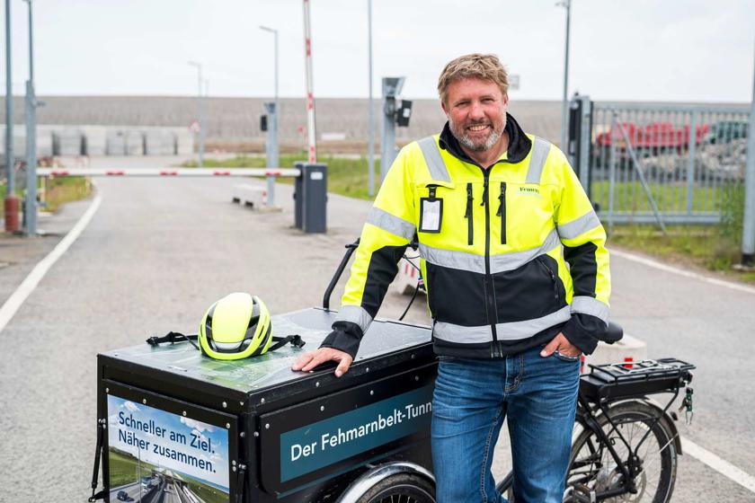 Citizen Manager Holger Marohn stands with his information cargo bike in front of the gate of the German construction site.
